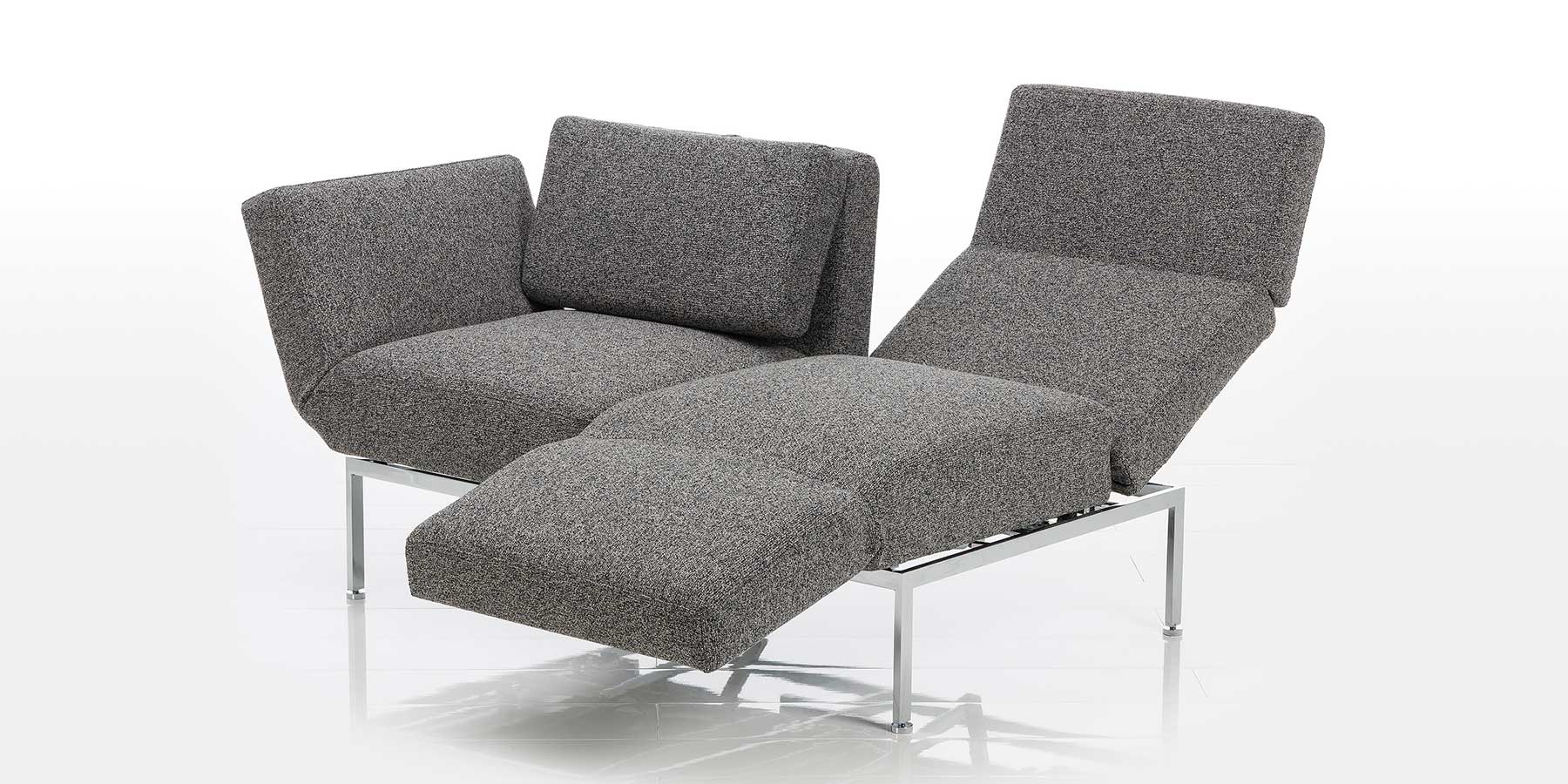 Multifunktionssofa in grauem Stoff. Die rechte Rückenlehne ist abgesenkt, die rechte Armlehne ist zur Fußstütze umgeschwenkt.