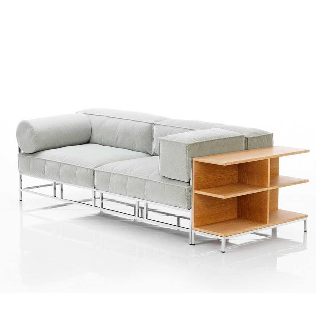 Sofa mit Polstern in hellem mint und chrom glänzendem Untergestell. Rechts neben dem Sofa ist ein niedriges, offenes Regal an das Sofa angestellt. 