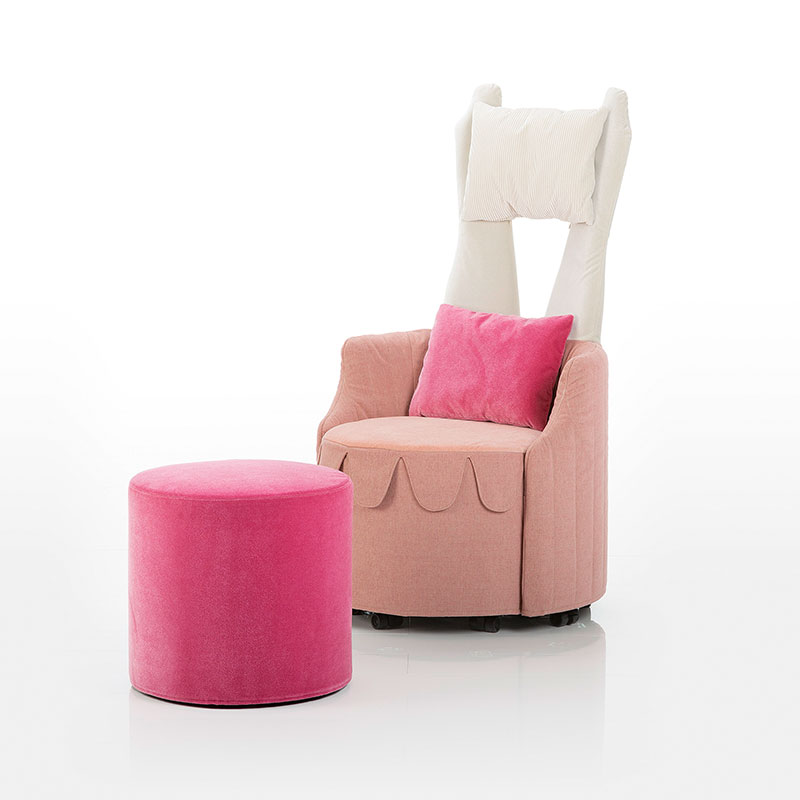 Highbackchair mit runder Sitzbasis in altrosa Stoff und mit zweigeteilter, mit weißem Stoff bezogener Rückenlehne. Auf dem Sessel ist ein Pinkes Kissen drappiert. Vor dem Sessel steht ein in pinkem Stoff bezogener Hocker mit runder Basis.