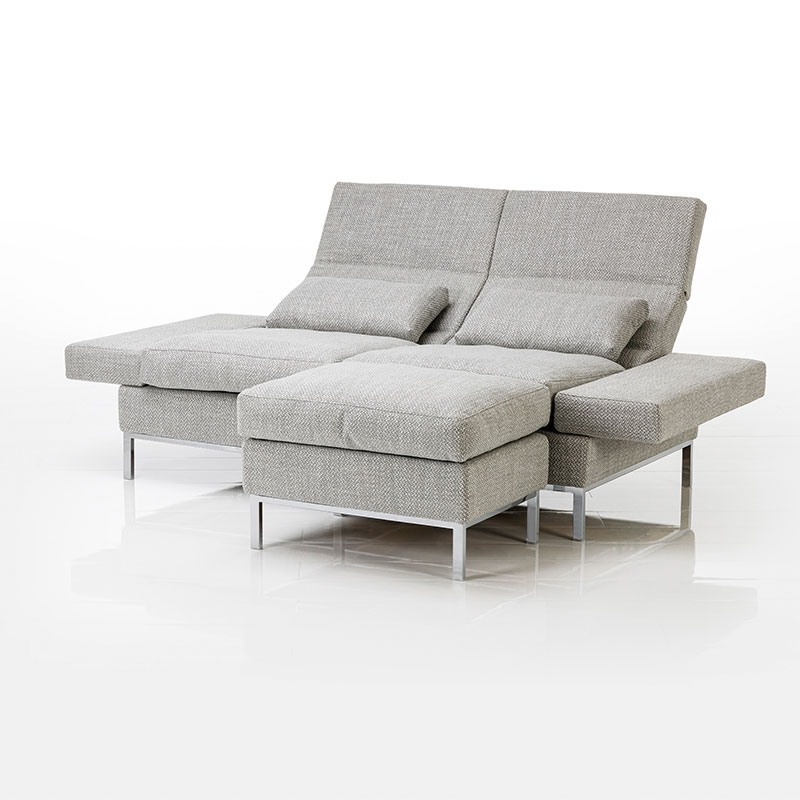 Hellgraues Sofa. Vor dem rechten Sitzplatz steht ein passender Hocker.