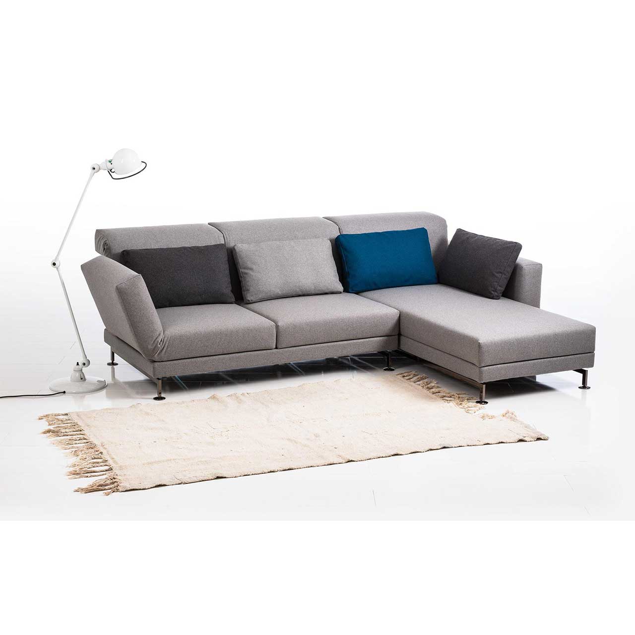 Eckgarnitur in grauem Stoff mit Longchair rechts, dekoriert mit vier Kissen in dunkelgrau, blau und hellgrau.
