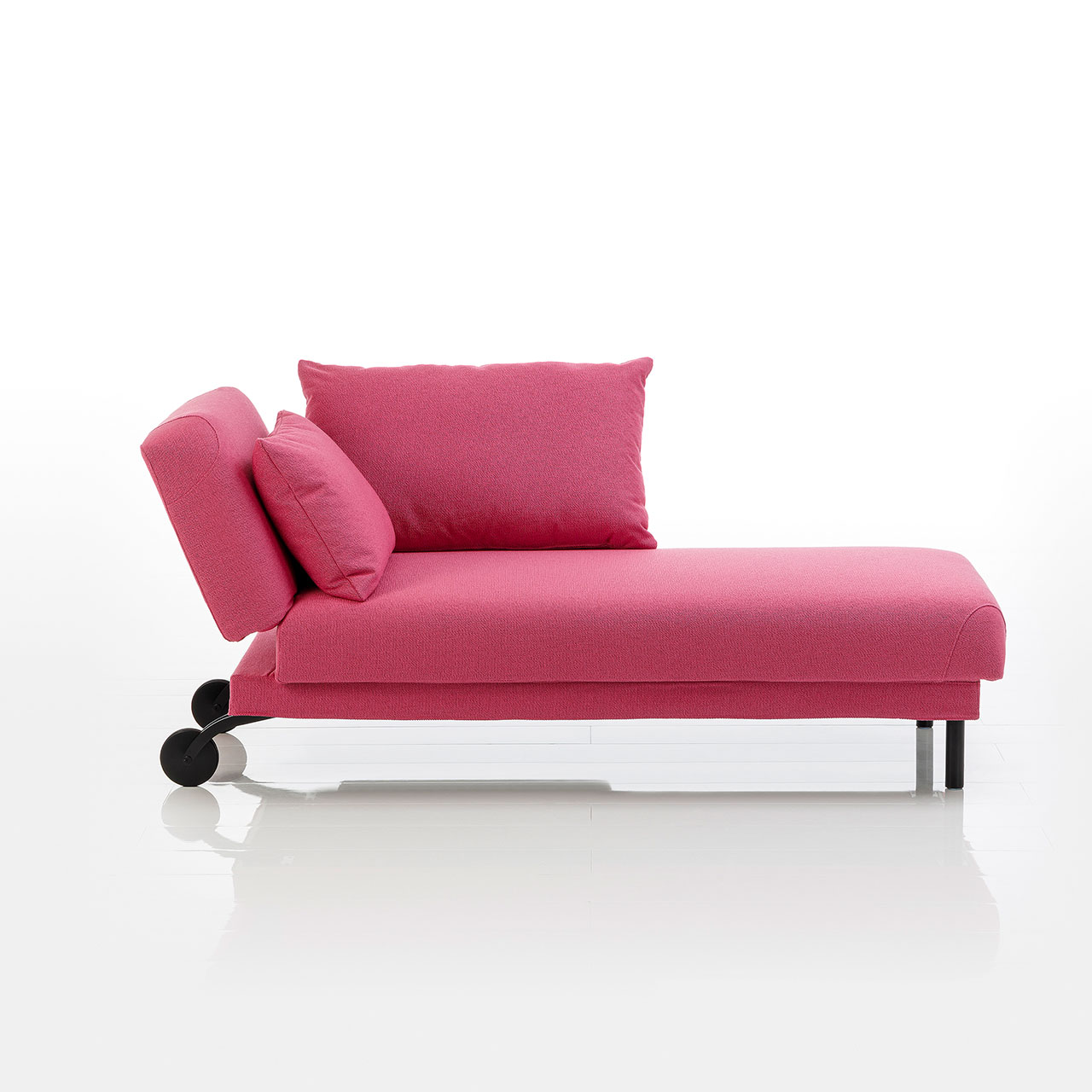 Recamiere in pinkem Stoff mit Rollen an der Kopfseite und zylindrischen Füßen an der Fußseite. Das Kopfteil ist höhenverstellbar. Rechts vom Kopfteil ist eine abklappbare Armlehne angebracht.