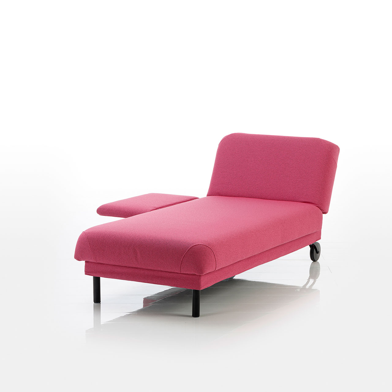 Recamiere in pinkem Stoff mit Rollen an der Kopfseite und zylindrischen Füßen an der Fußseite. Das Kopfteil ist höhenverstellbar. Die Armlehne links vom Kopfteil ist abgeklappt.