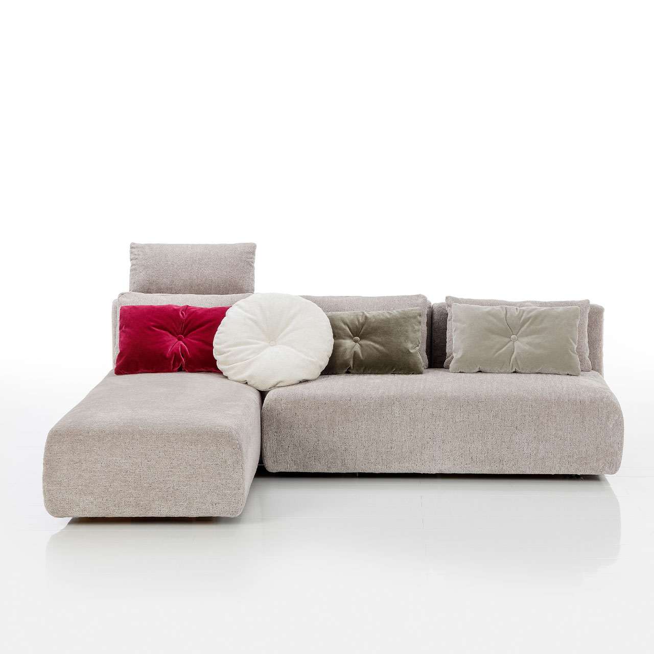 Bodennahes beiges Eckofa mit Longchair links und Drehsofa rechts. Auf dem Sofa liegen drei eckige und eine rundes Kissen.