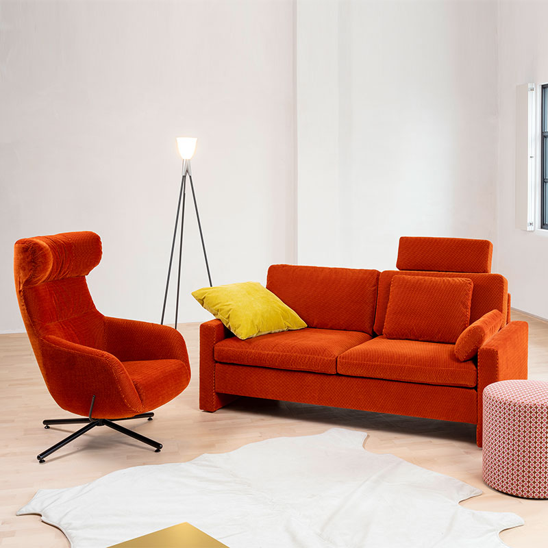 Ambientebild mit einer Couch in rostrot und einem Drehsessel in gleicher Farbe.