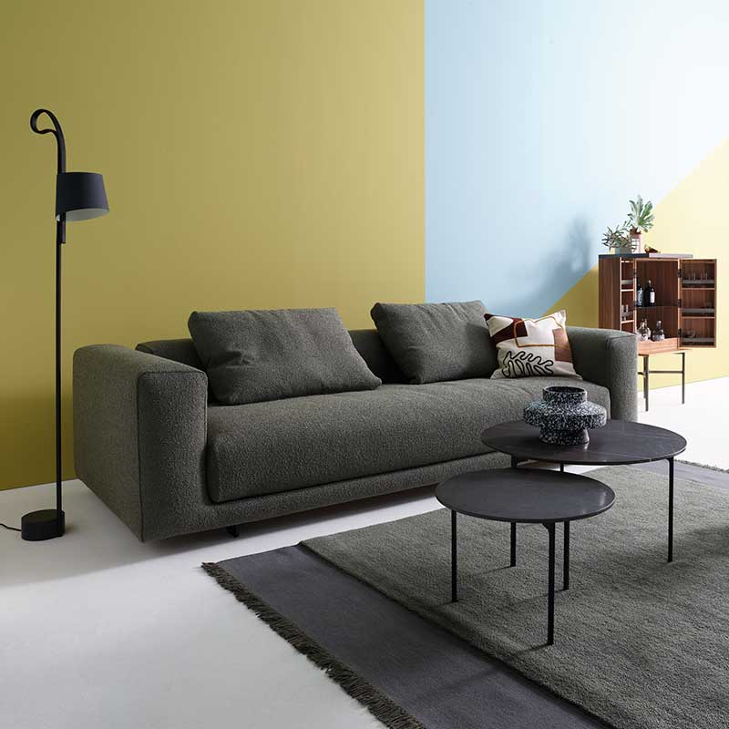 Sofa aus graugrünem Stoff mit zwei Kissen darauf in einem Wohnzimmer mit Dekoration
