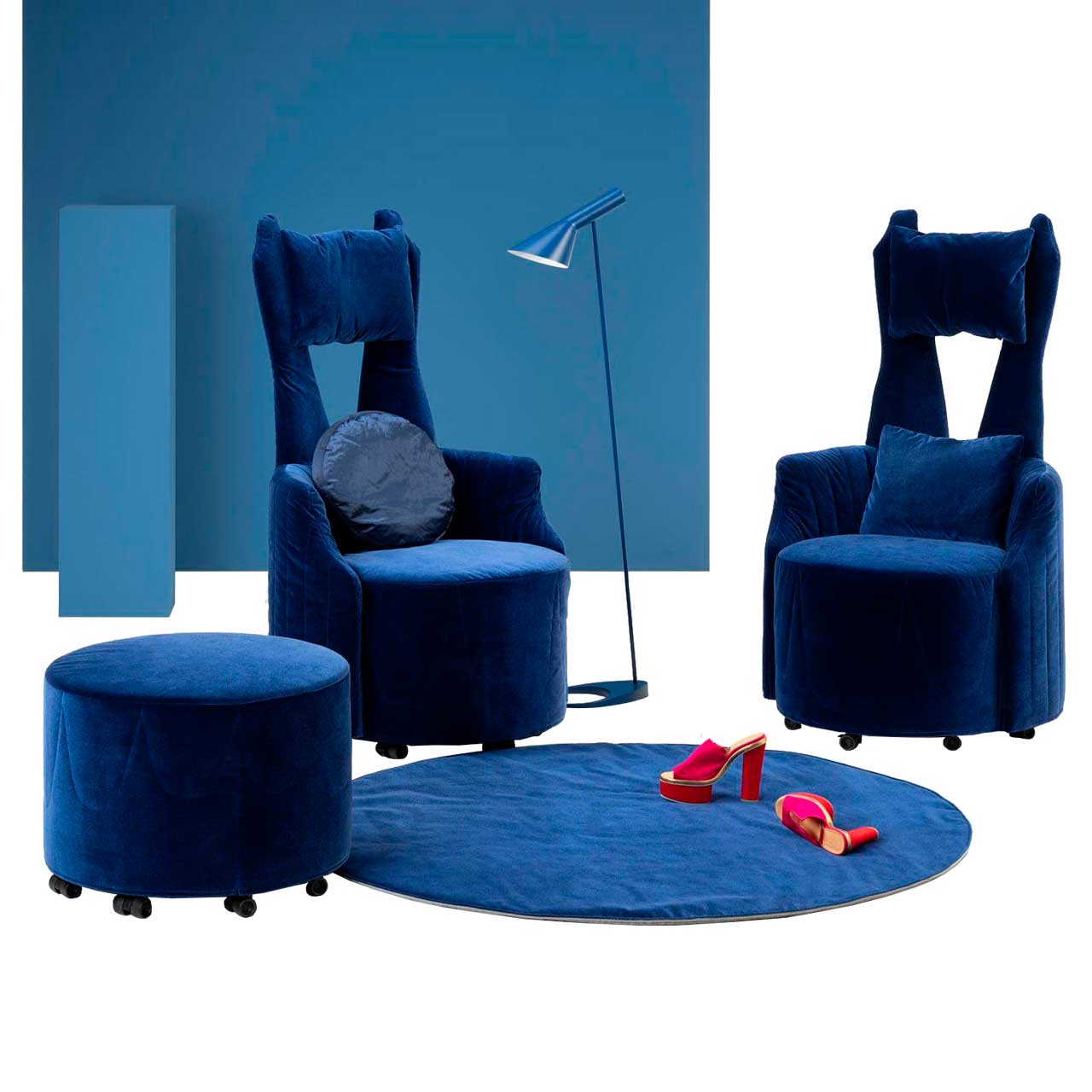 Ambientebild: Zwei dunkelblaue Highbackchairs mit zweigeteilter Rückenlehne stehen um einen runden, dunkelblauen Teppich. Vorne rechts steht ein passender Hocker.