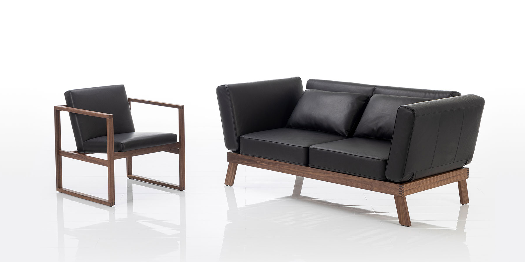 Ein zweisitziges Sofa mit Holzgestell aus dunklem Holz. Die Polster sind mit schwarzem Leder bezogen.