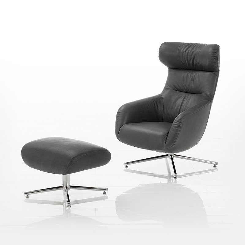 Schwarzer Drehsessel mit Kreuzfuß und mit Armlehnen. Vor dem Sessel steht ein passender Hocker.