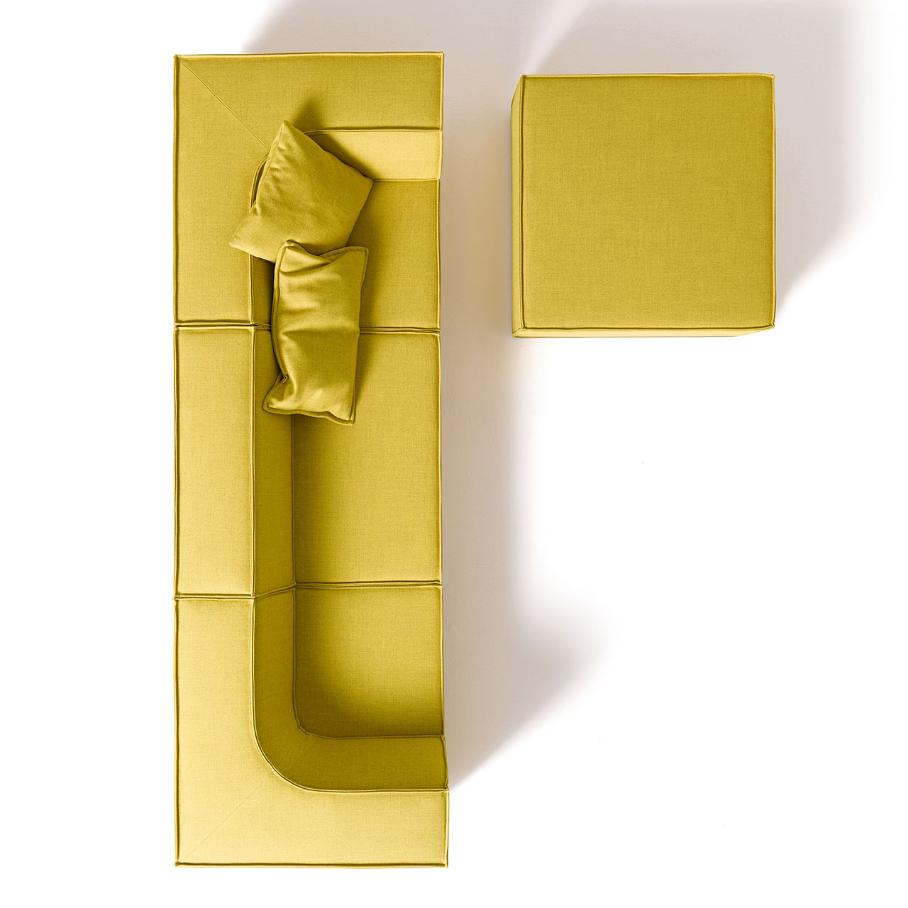 Gelbes Sofa bestehend aus drei Sitzelementen und drei Rückenteilen mit einem weiteren quadratischen Sitzelement als Hocker davor. Farbe gelber Stoff.