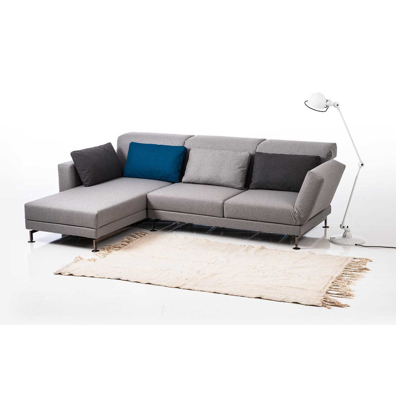 Eckgarnitur in grauem Stoff mit Longchair links, dekoriert mit vier Kissen in dunkelgrau, blau und hellgrau.