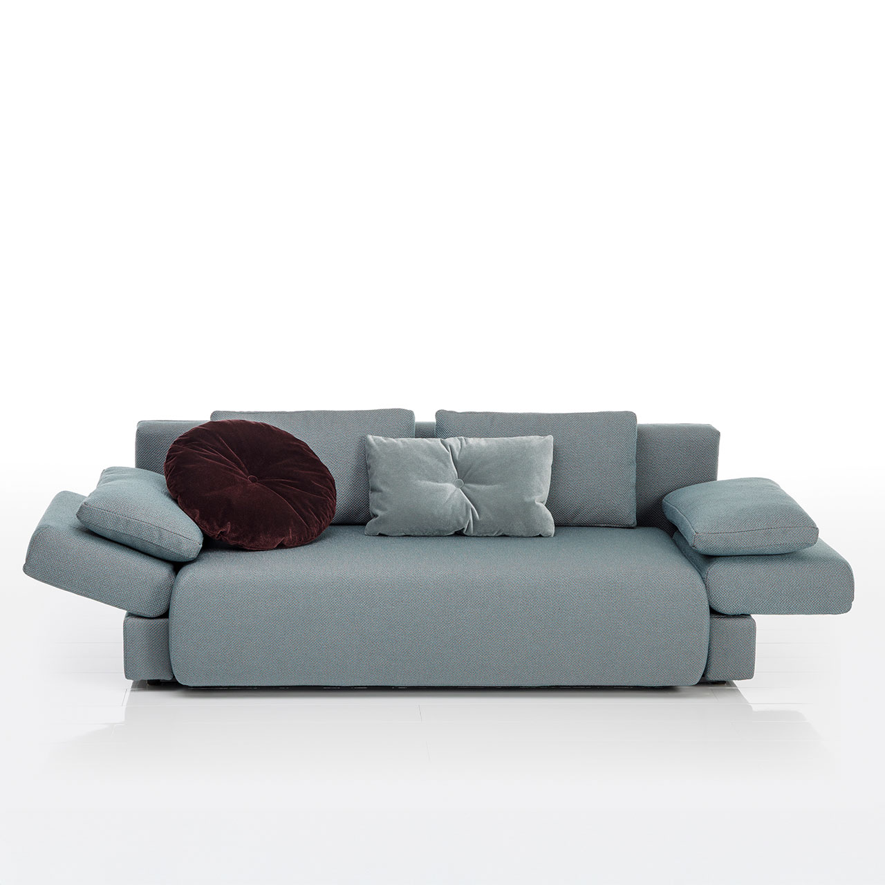 Bodennahes grau-grünes Sofa mit drei eckigen und einem runden Kissen. Die Armlehnen sind abgeklappt.