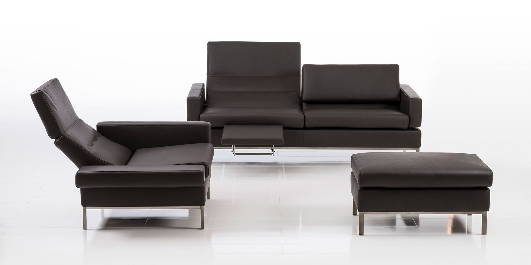 Eine Polsterkombination bestehend aus einer 2-sitzigen Couchm einem Sessel mit abgesenkter Rückenlehne und einem Hocker in dunkelbraunem Leder.