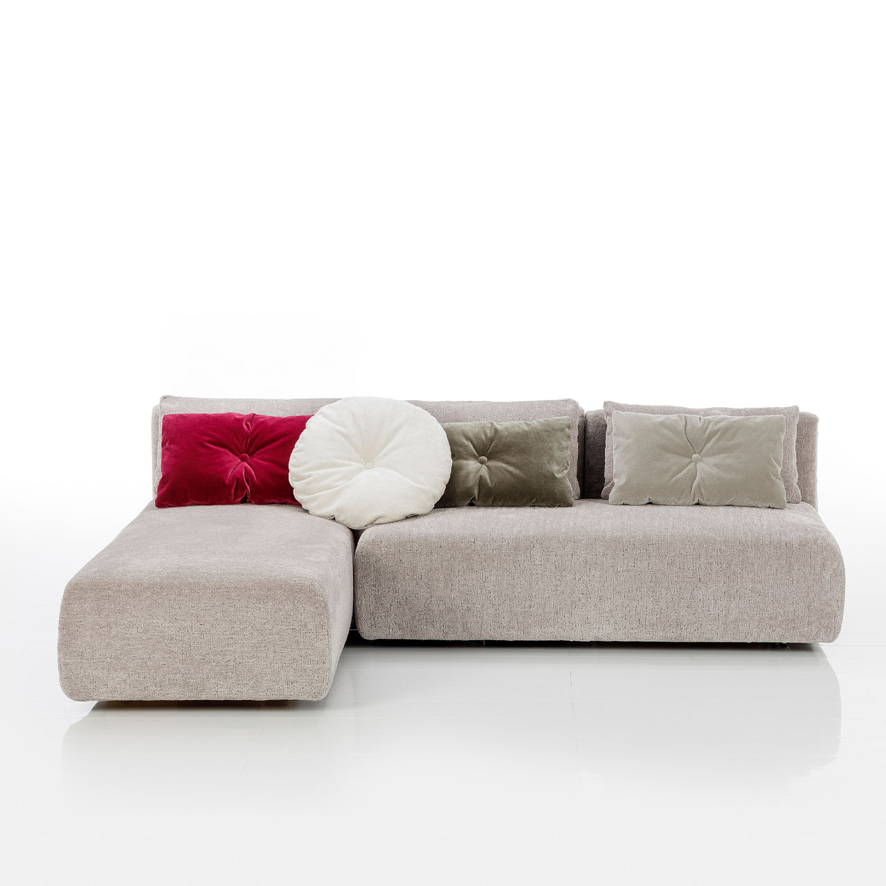 Bodennahes beiges Eckofa mit Longchair links und Drehsofa rechts. Auf dem Sofa liegen drei eckige und eine rundes Kissen.