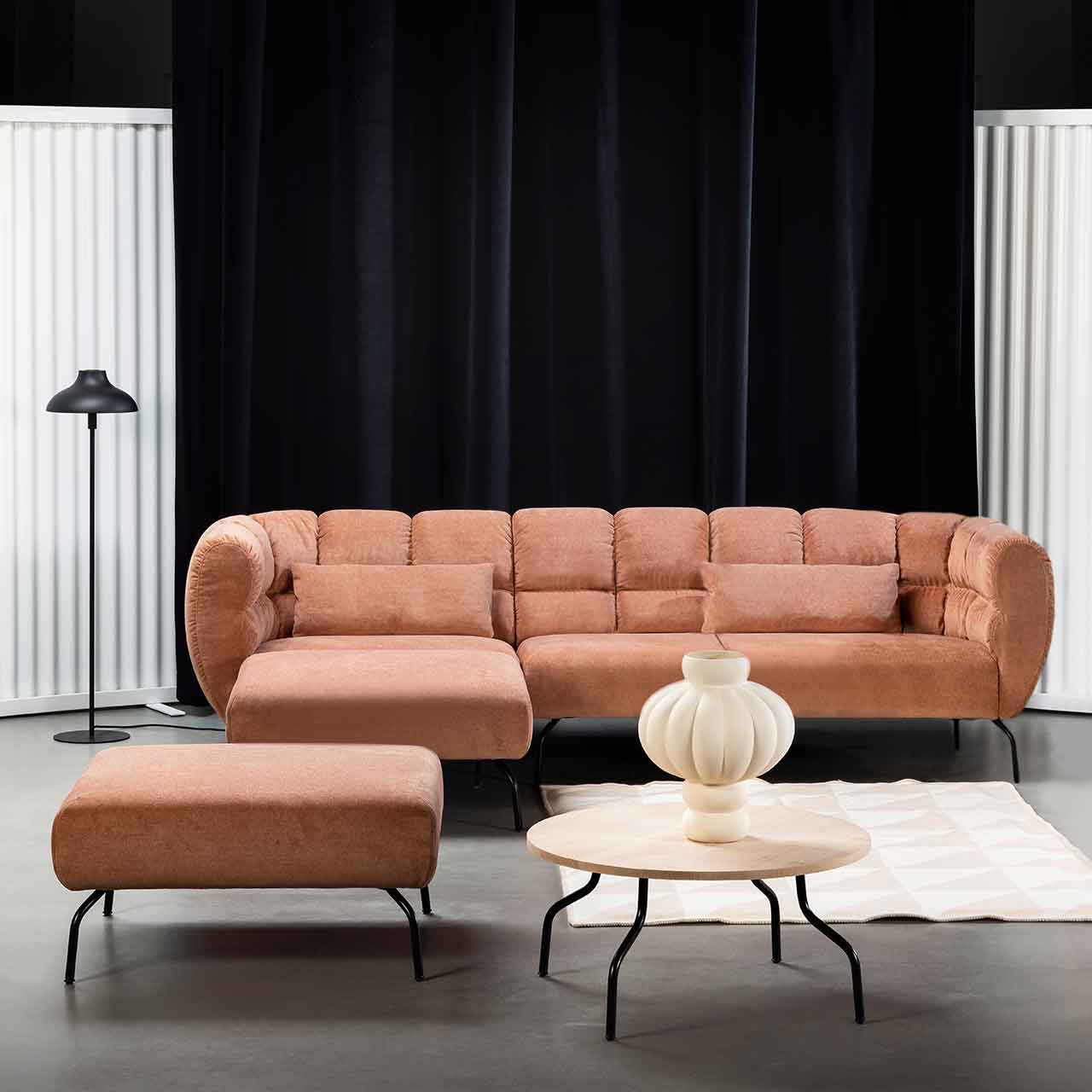 Eckgarnitur von brühl magnolia mit Longchair links in rotbraunem Leder mit schwarzen Füßen. Links vor der Garnitur steht ein quadratischer Hocker. Zentral vor der Garnitur steht ein runder Beistelltisch mit heller Holzplatte.