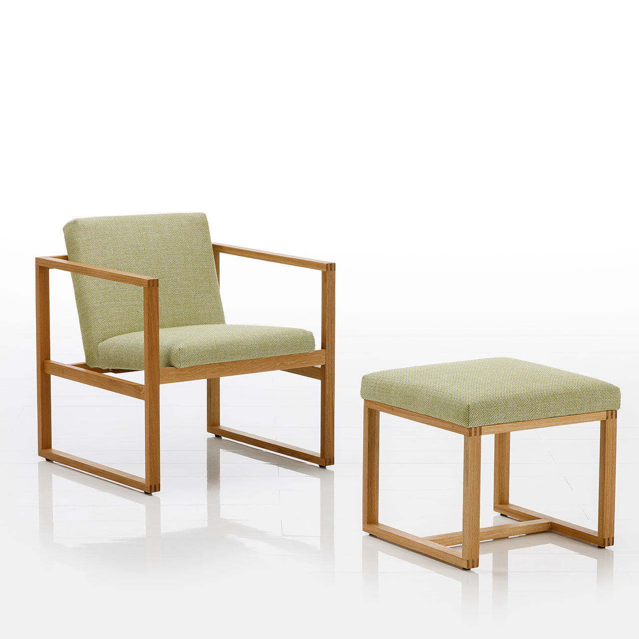 Ein Sessel mit niedriger Rückenlehne und ein passender Hocker. Beide Möbel sind mit einem limettengrünen Stoff bezogen. Die Untergestelle sind aus einem warmen Holz.