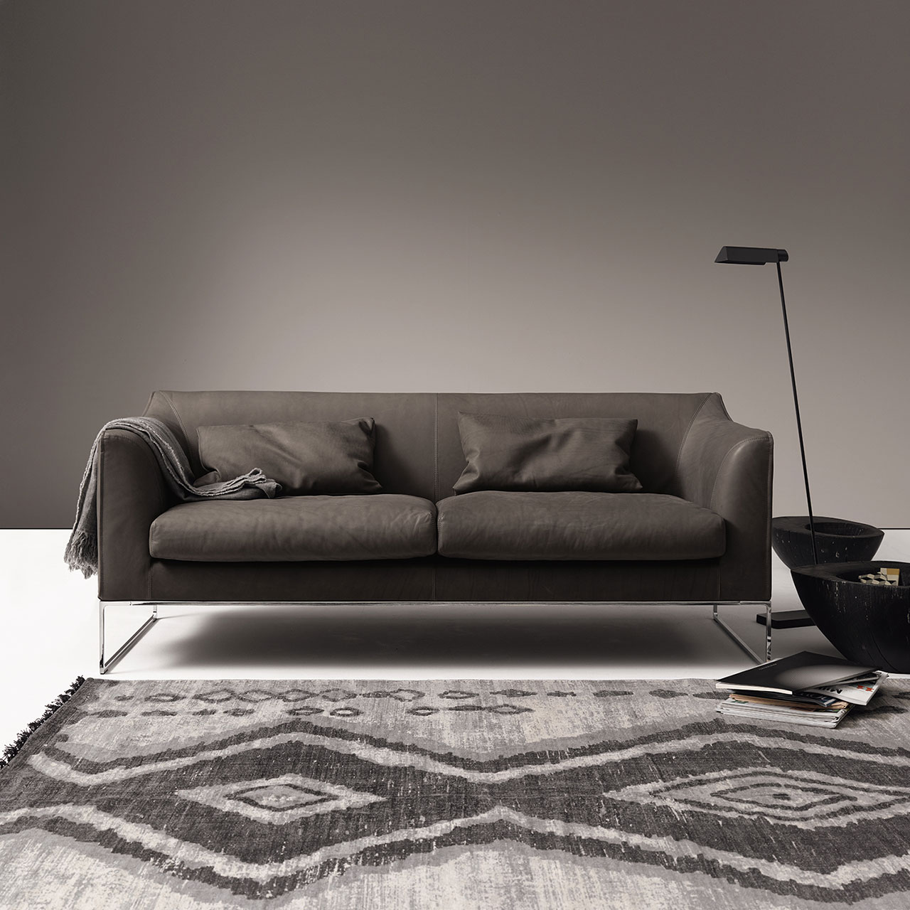 Sofa mit leicht erhöhtem Rücken mit zwei Kissen und Decke in einem Wohnzimmer