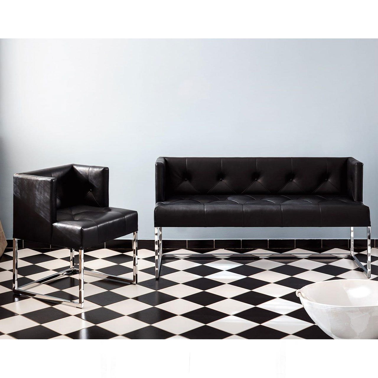Ambientebild: Sessel der Serie belami low und passende Polsterbank in schwarzem Leder auf einem schwarz-weiß gefliesten Boden und vor einer weißen Wand.