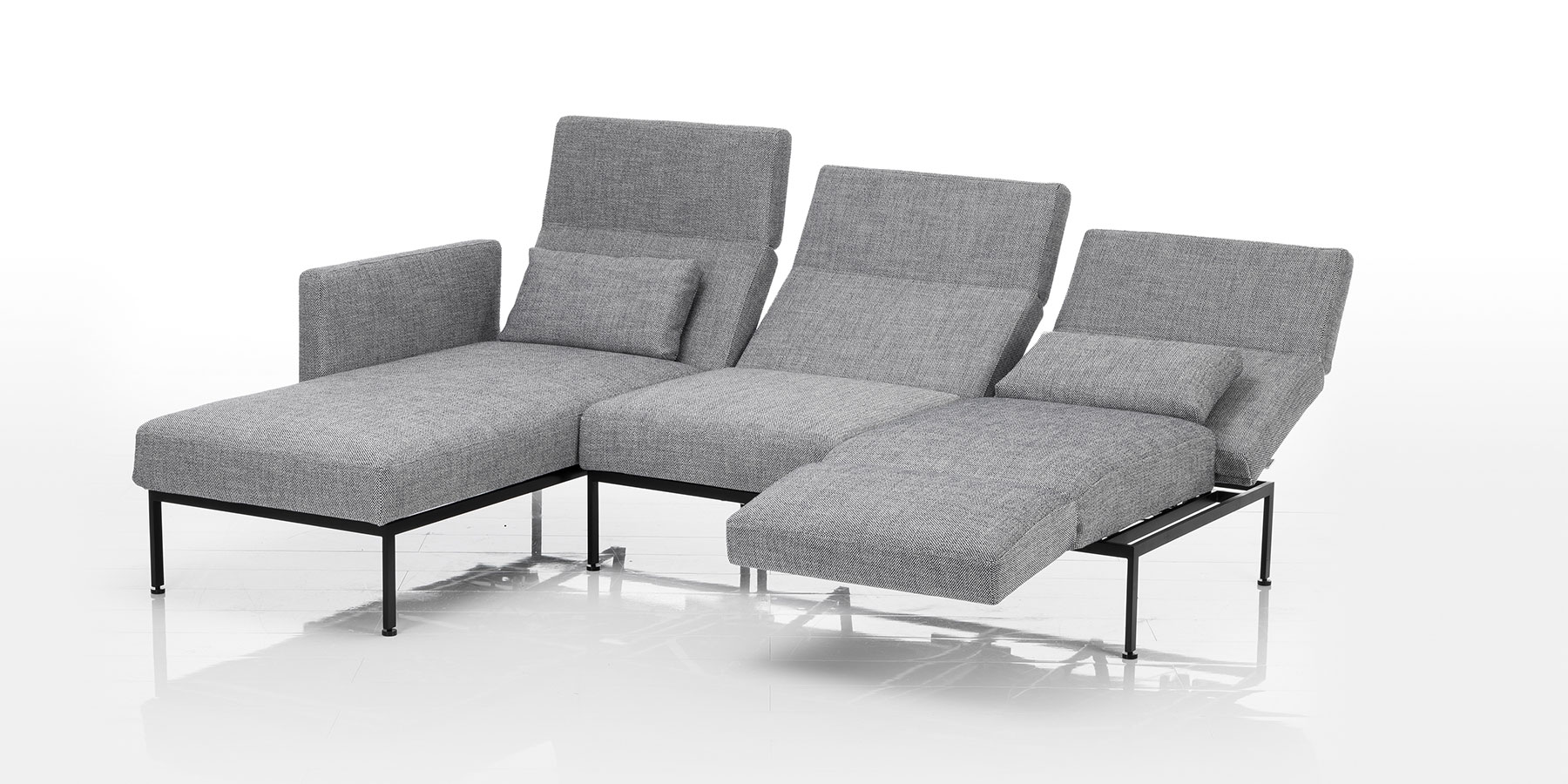 Eine Eckkombination aus einer Recamiere und einem zweisitzigen Anstellsofa in grauem Stoff. Das Untergestell ist aus schwarzem Metall.