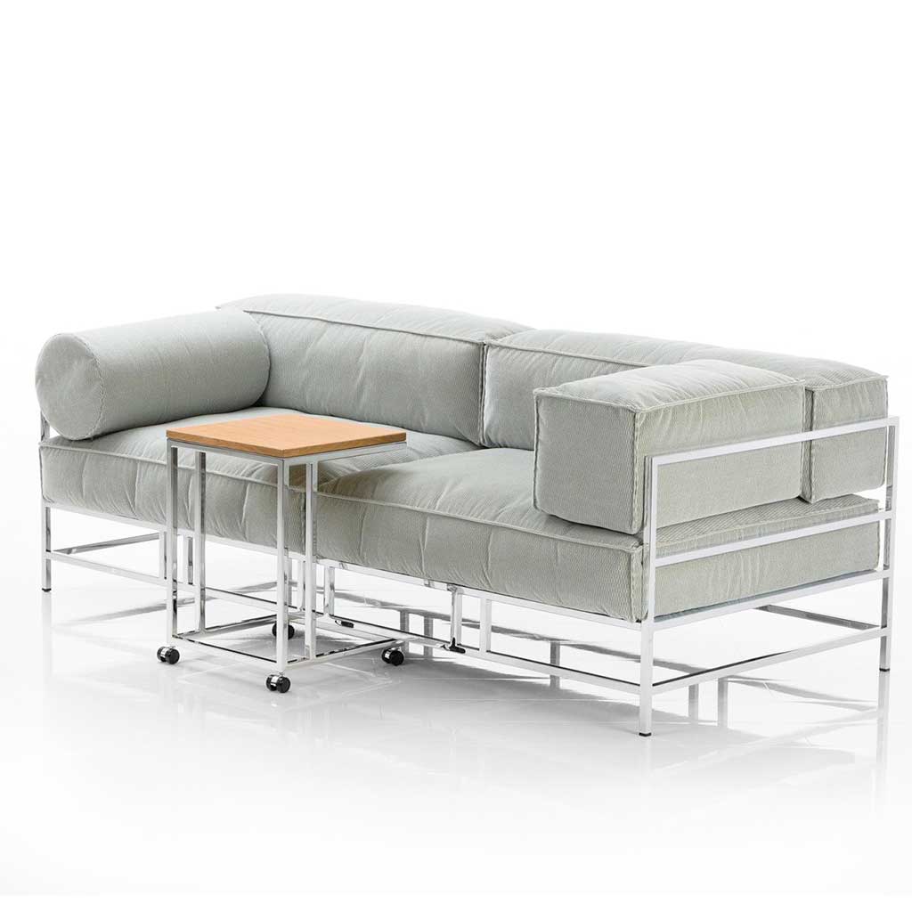 Sofa mit Polstern in hellem mint und chrom glänzendem Untergestell. Vor dem Sofa steht ein kleiner Beistelltisch auf Rollen.