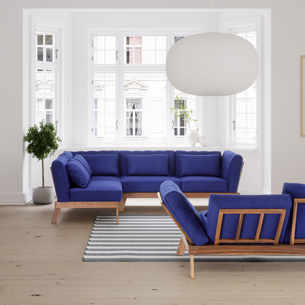 Ambientebild. Zwei Eckgarnituren der Serie brühl lofoten pure mit Untergestell aus heller Eiche und Polstern in königsblau vor einem breiten Altbaufenster.