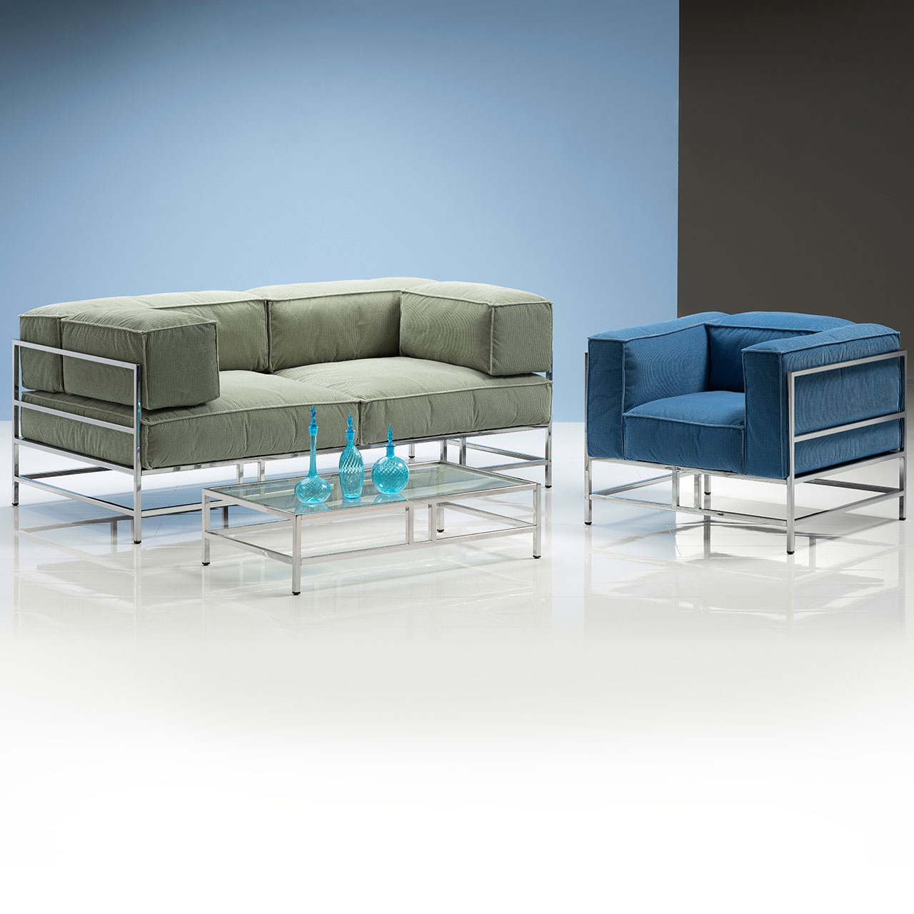 Sessel mit hellblauen Polstern und mit chrom glänzendem Untergestell. Links davon steht ein Sofa mit hellgrünen Polstern und ebenfalls chrom glänzenden Untergestell.