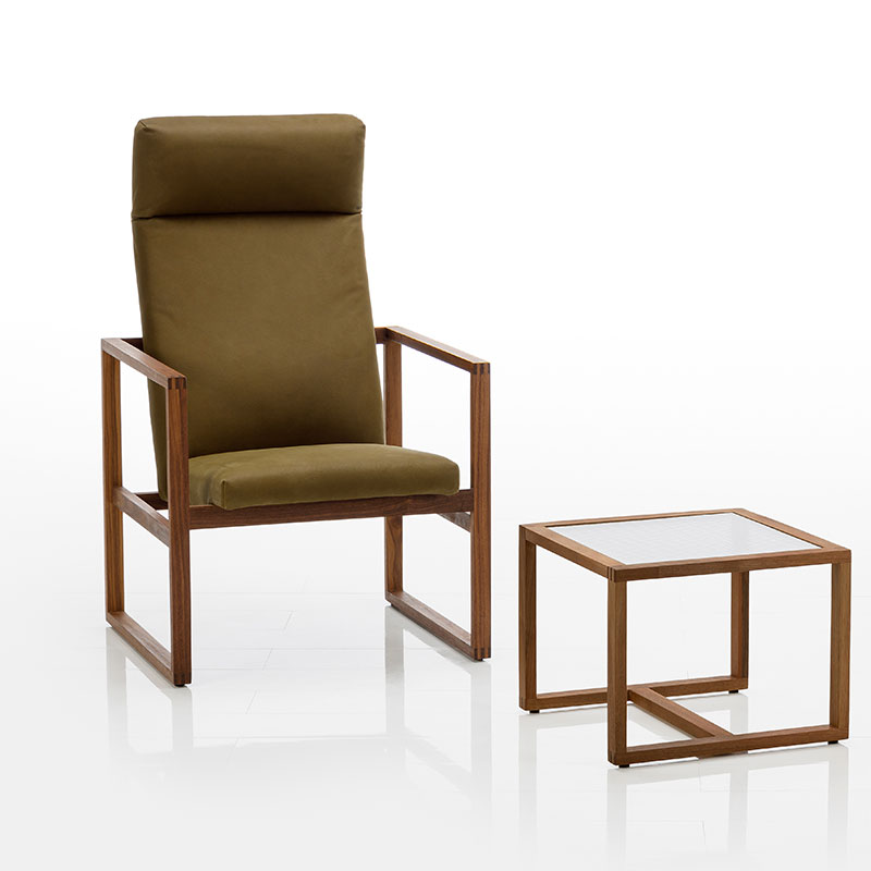 Ein Sessel mit Holzrahmen in dunkler Eiche. Die Sitzfläche ist mit dunkelgrünem Stoff bespannt. Daneben steht ein Beistelltisch mit einer Glasplatte.