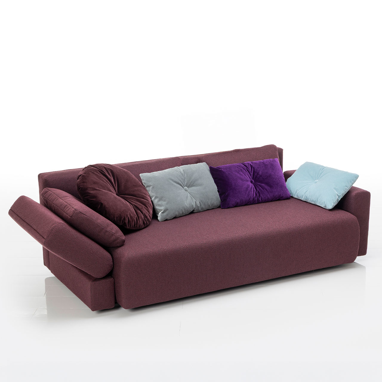 Bodennahes weinrotes Sofa mit drei eckigen und einem runden Kissen. Die linke Armlehne ist abklappbar.