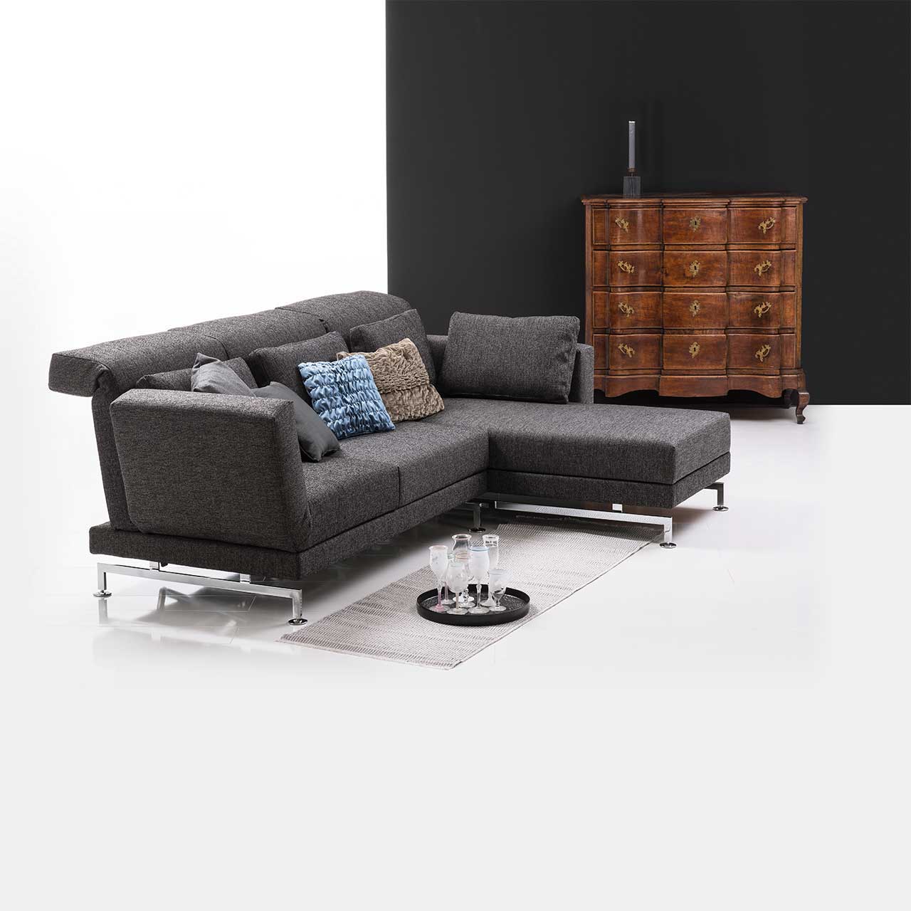 Eckgarnitur in grauem Stoff mit Longchair links, dekoriert mit bunten Kissen. .