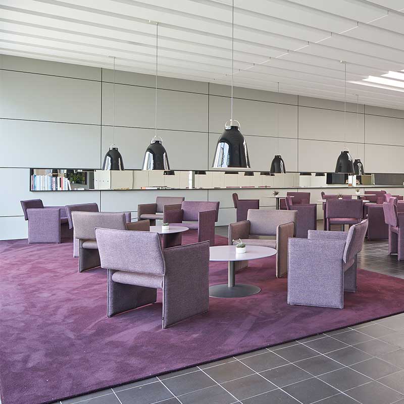 Viele COR Noto Sessel und Stühle um runde Tische gruppiert in Bistro-Atmosphäre