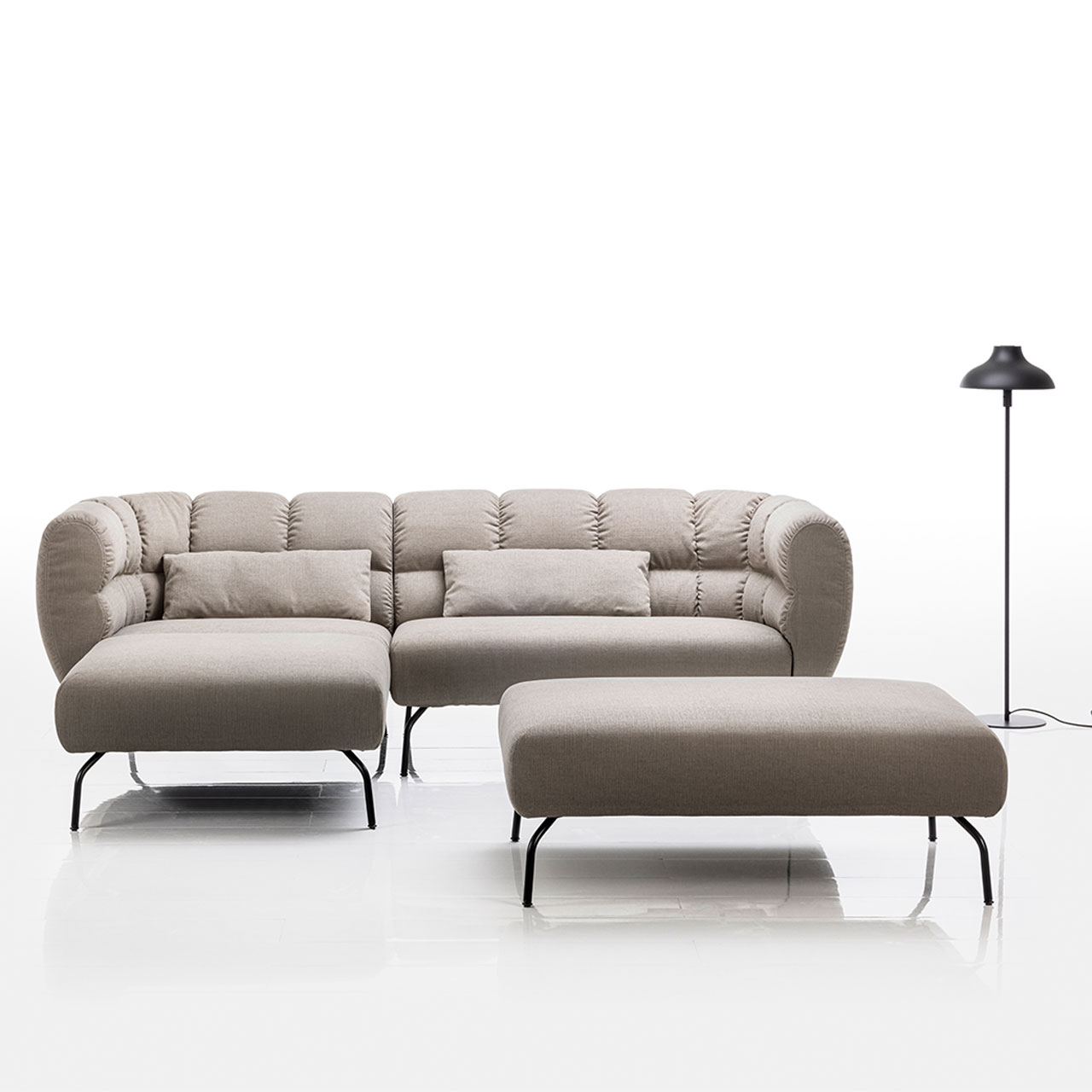 Ambientebild: Eckgarnitur von brühl magnolia mit Longchair links in grauem Leder mit schwarzen Füßen. Rechts vor der Garnitur steht eine Bank.