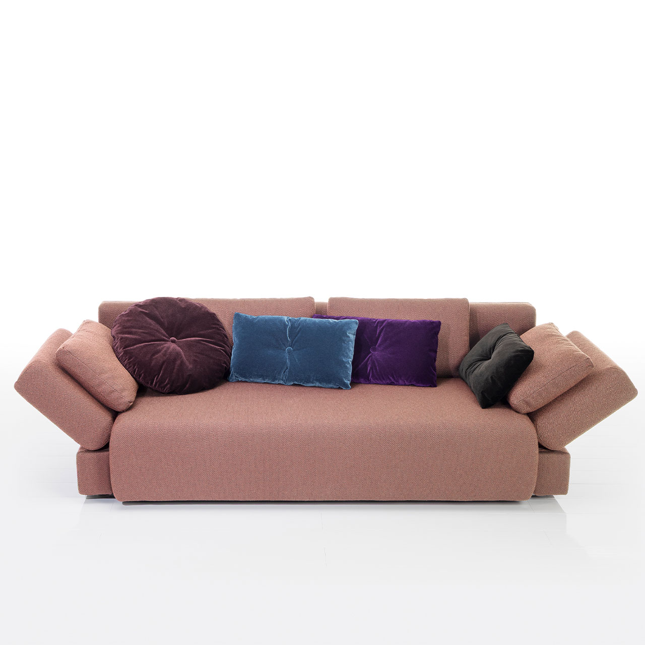 Bodennahes altrosa Sofa mit drei eckigen und einem runden Kissen. Die Armlehnen sind im 45 Grad abgeklappt.
