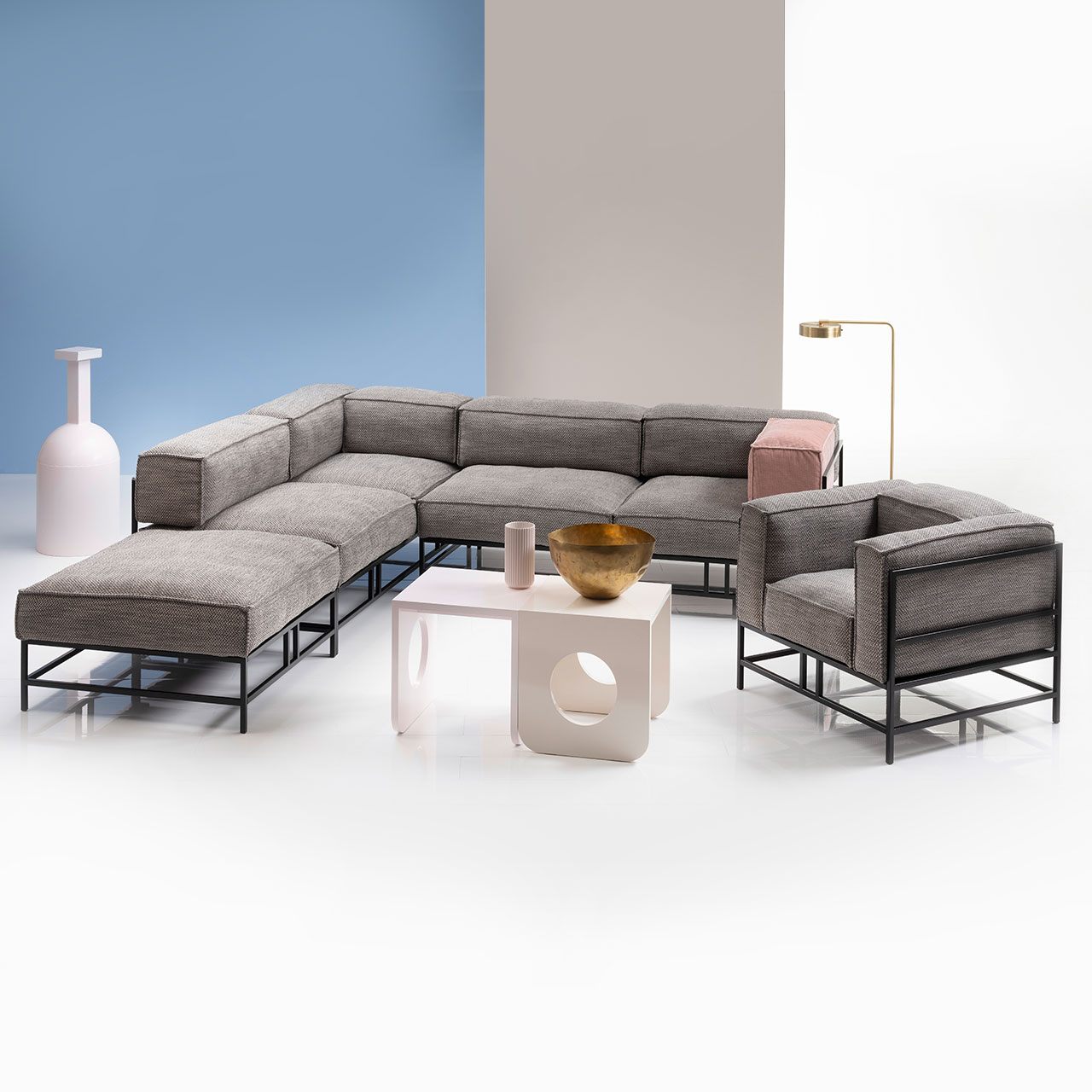 Ambientebild: L-förmige Garnitur mit hellen Polstern und schwarzem Untergestell. Rechts der Garnitur steht ein passender Sessel. Vor dem Ensemble steht ein weißer Couchtisch.