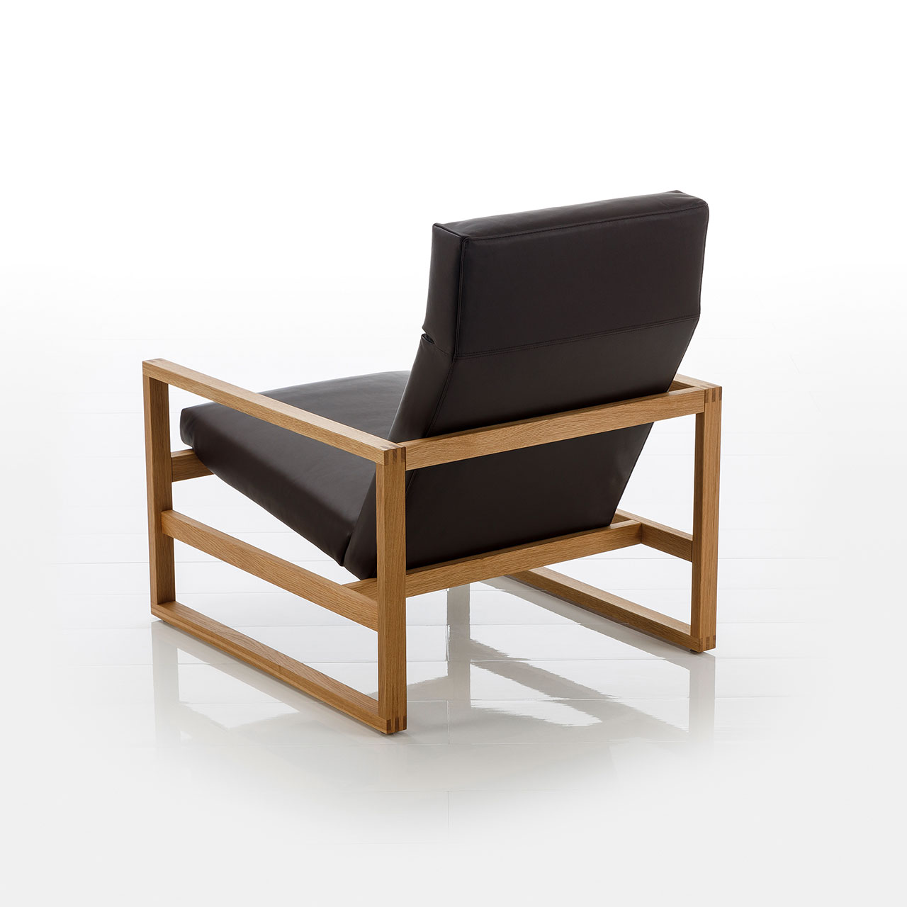 Rücksicht auf einen niedrigen Lounge-Sessel mit Holzgestell in heller Eiche. Die Sitzfläche ist mit schwarzem Leder bezogen.