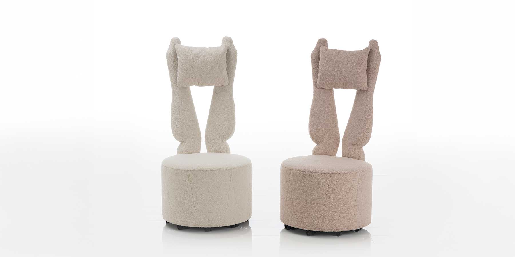 Zwei Hochlehnsessel mit runder Sitzbasis und gegabelter Rückenlehne. Der linke Sessel ist in einem cremeweißen Stoff, der rechte in einen pastellrosa Stoff bezogen.