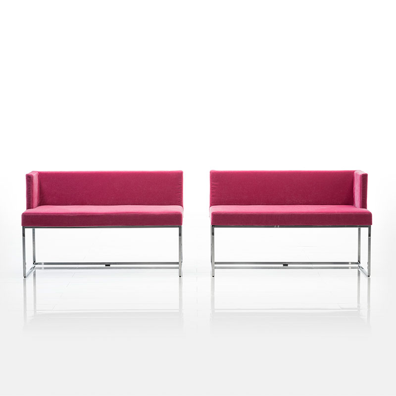 Zwei kurze Bänke mit niedriger Rücken- und je einer Armlehnen in schwarzem Leder stehen direkt nebeneinander. Die offenen Seiten sind innen.  