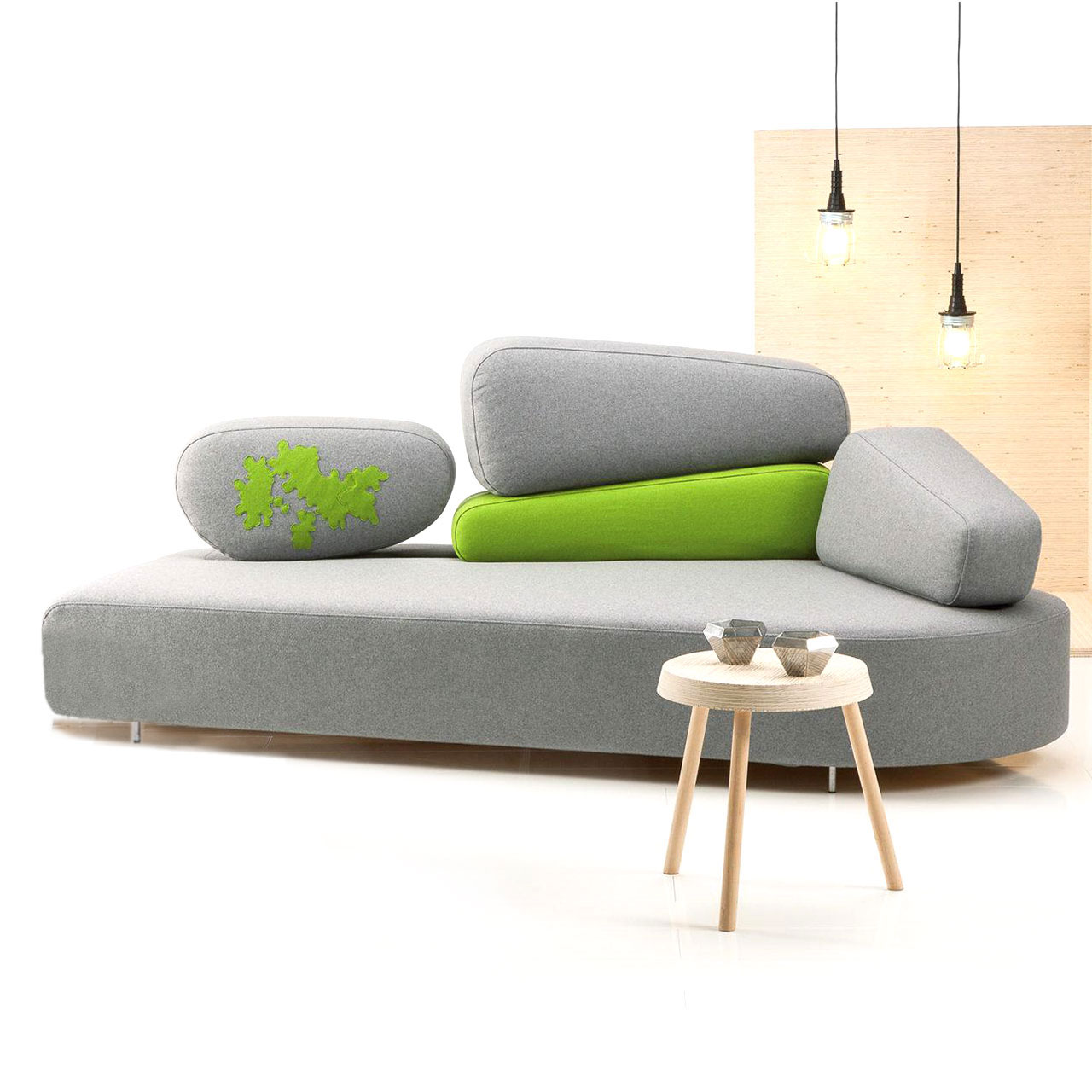 Graues asymmetrisches Sofa. Der Rücken besteht aus vier einzelnen, ebenfalls asymmetrischen Elementen. In der Mitte zwei Elemente übereinander, rechts und links jeweils ein Element. Das Element in der Mitte unten ist hellgrün bezogen.