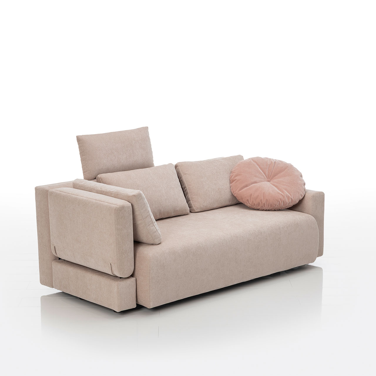 Bodennahes beiges Sofa mit drei eckigen und einem runden Kissen. Die linke Armlehne ist abklappbar.