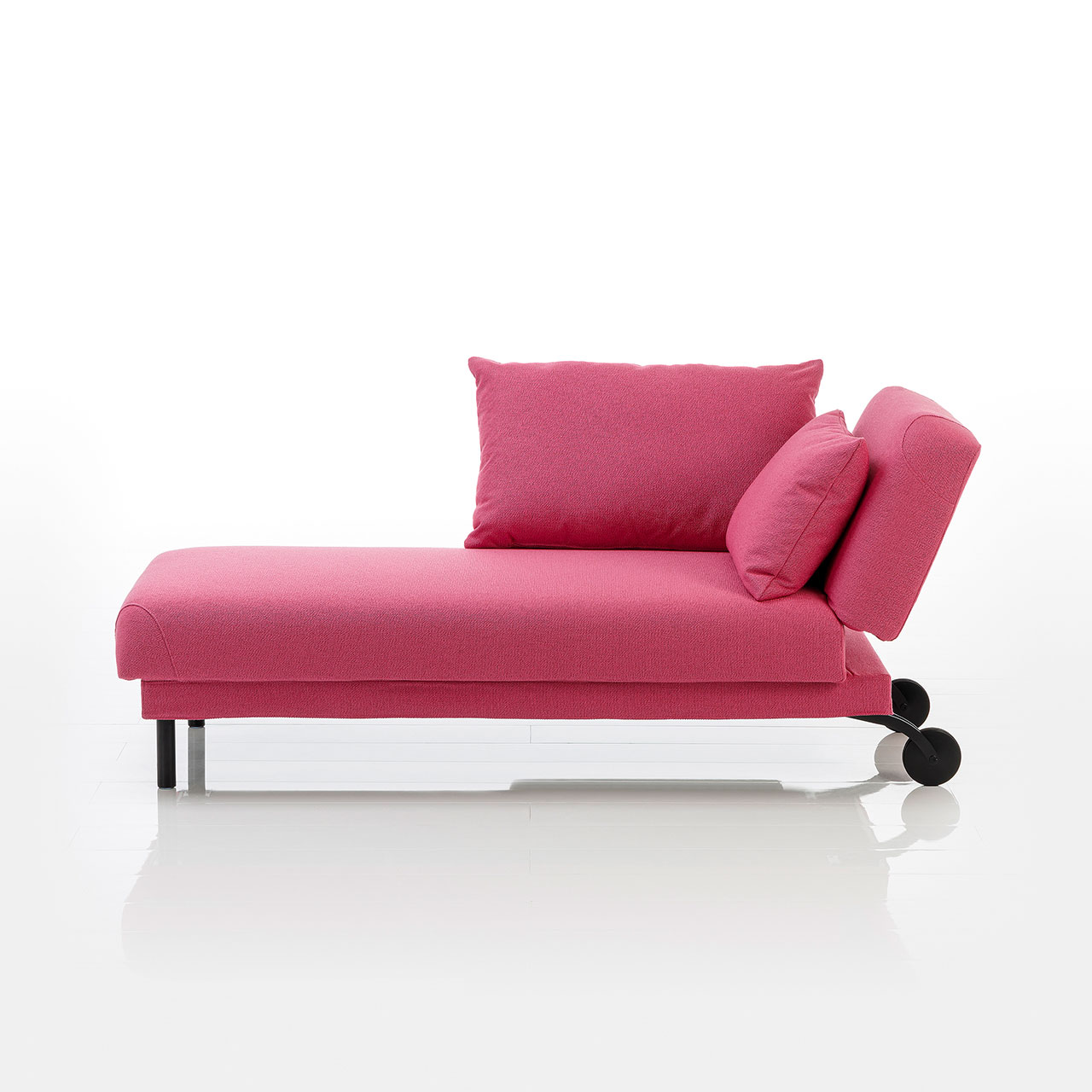 Recamiere in pinkem Stoff mit Rollen an der Kopfseite und zylindrischen Füßen an der Fußseite. Das Kopfteil ist höhenverstellbar. Links vom Kopfteil ist eine abklappbare Armlehne angebracht.