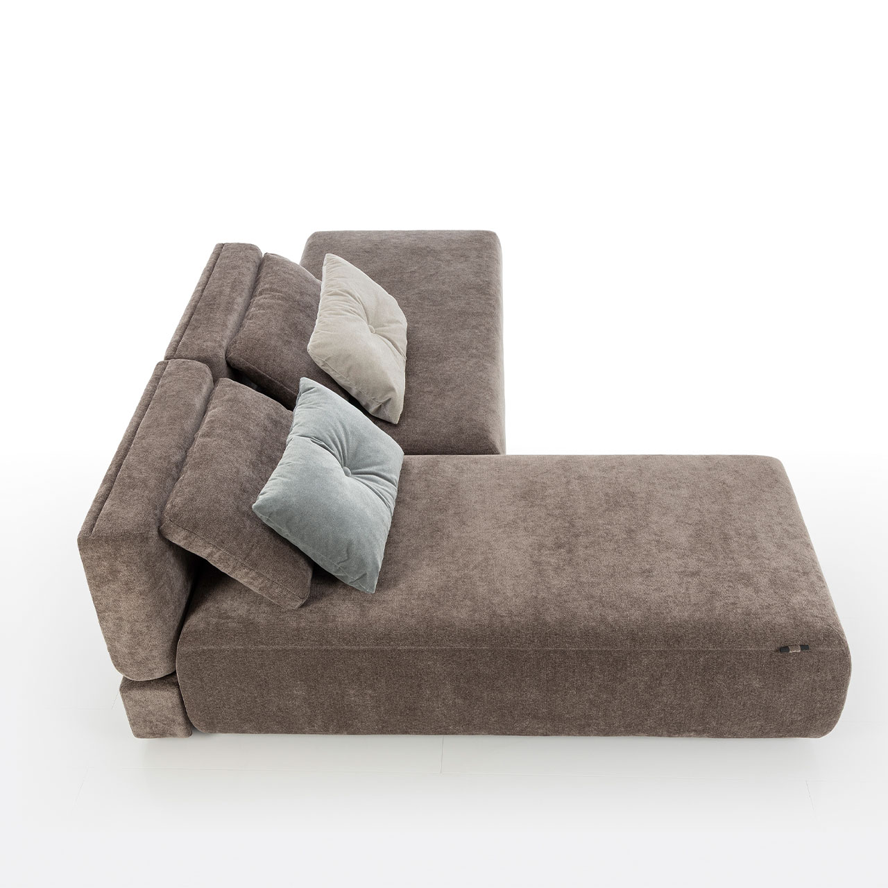 Bodennahes braunes Eckofa mit Longchair links und Drehsofa rechts. Auf dem Sofa liegen zwei eckige Kissen.