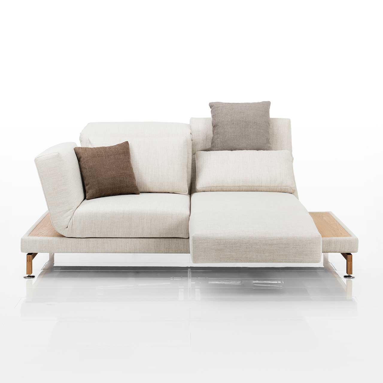 Cremeweißes Sofa. Rechts und links neben den Armlehnen befinden sich schmale Ablageflächen in hellem Holz. Die rechte Armlehne ist als Fußstütze vorgeschwenkt, die Rückenlehne leicht abgesenkt.