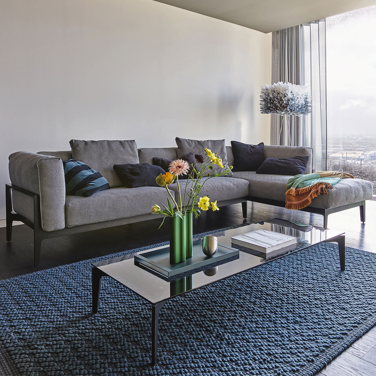 Milieuaufnahme einer Eckkombination aus Sofa-Element mit Lehne links und Recamiere rechts mit grauem Stoffbezug auf Holzgestell.