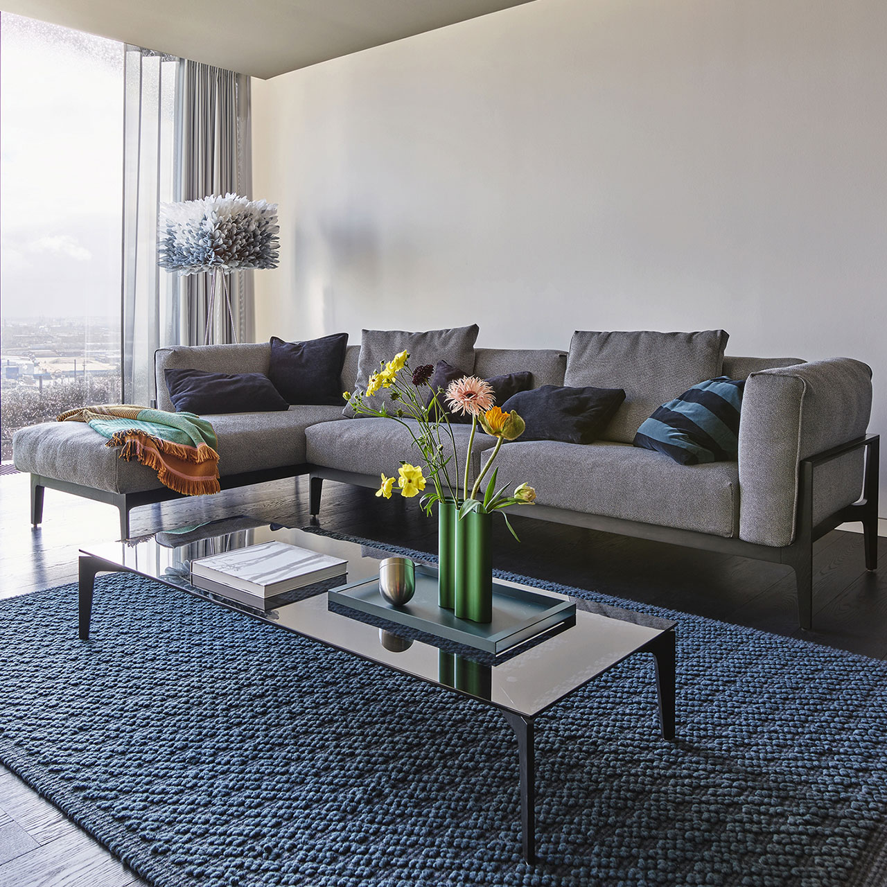 Milieuaufnahme einer Eckkombination aus Sofa-Element mit Lehne rechts und Recamiere links mit grauem Stoffbezug auf Holzgestell.