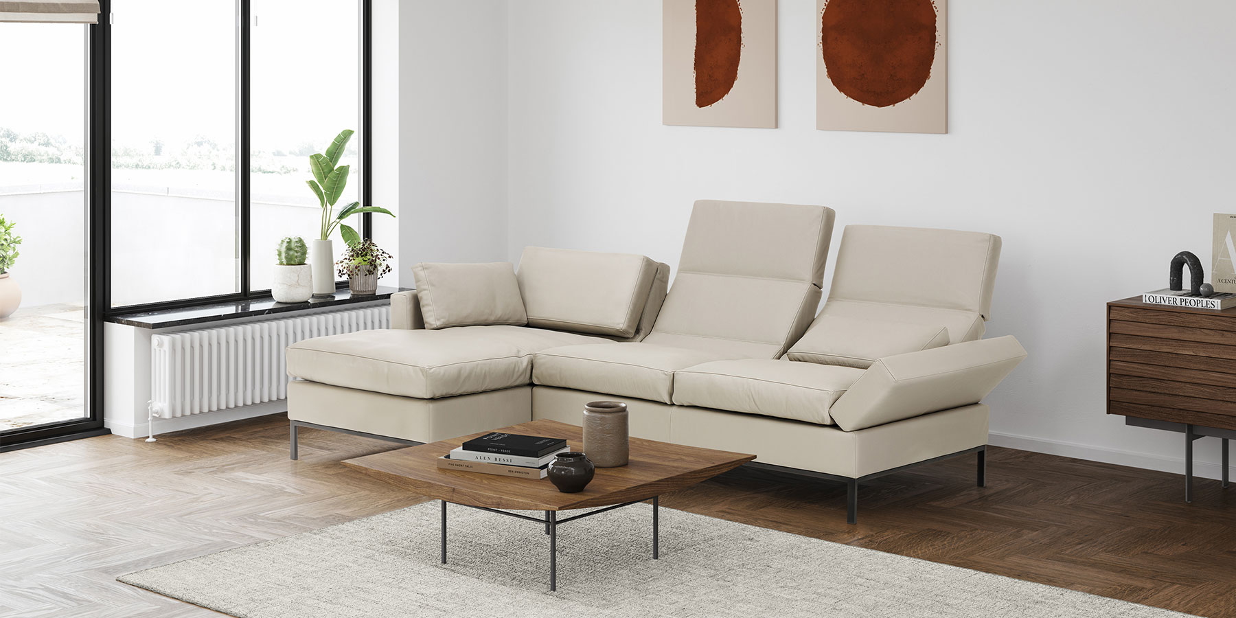 Cremefarbene Eckgarnitur. Die Rückenlehnen sind teilweise zur Relaxposition abgesenkt. Davor steht ein filigraner Beistelltisch in dunklem Holz.