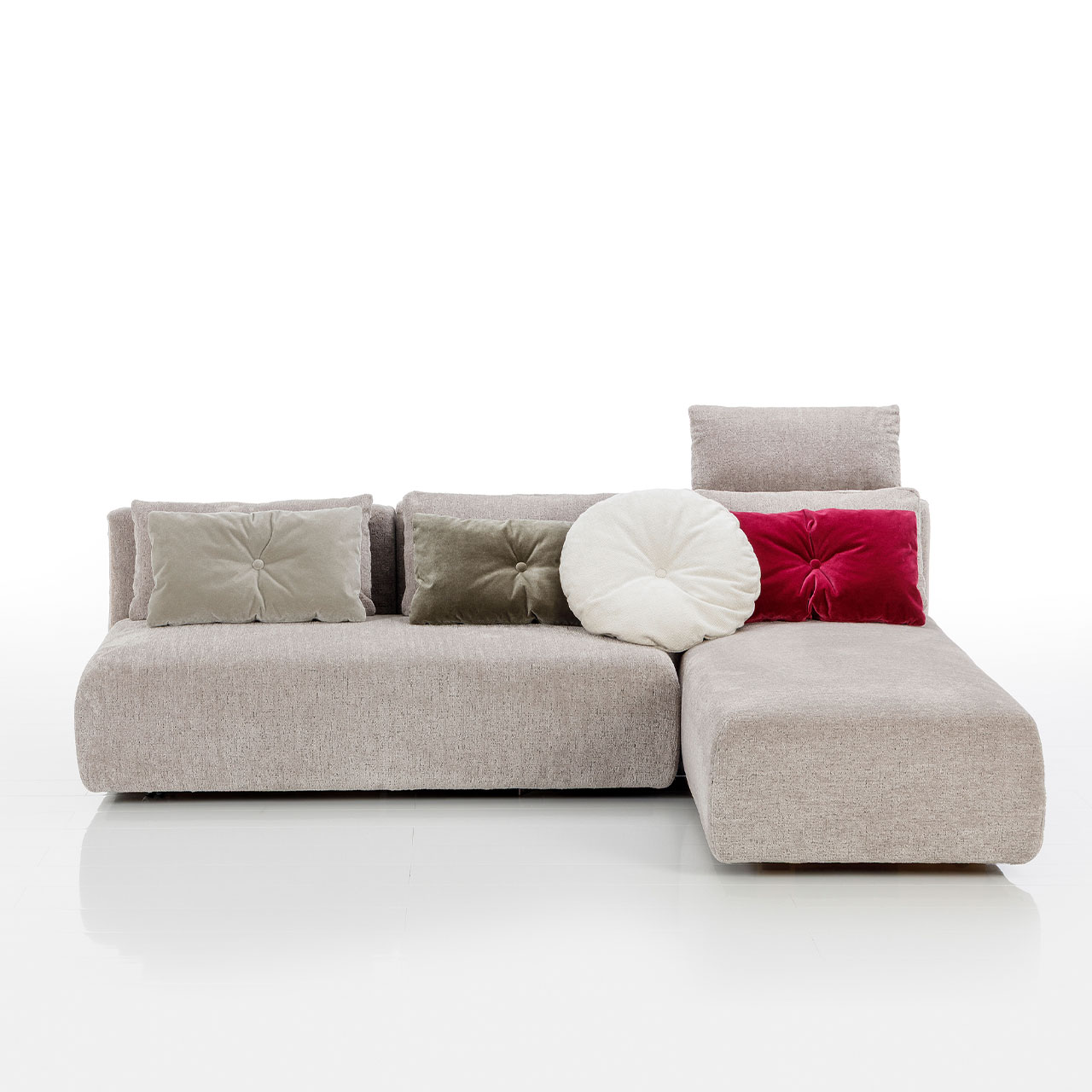 Bodennahes beiges Eckofa mit Drehsofa links und Longchair rechts. Auf dem Sofa liegen drei eckige und eine rundes Kissen.