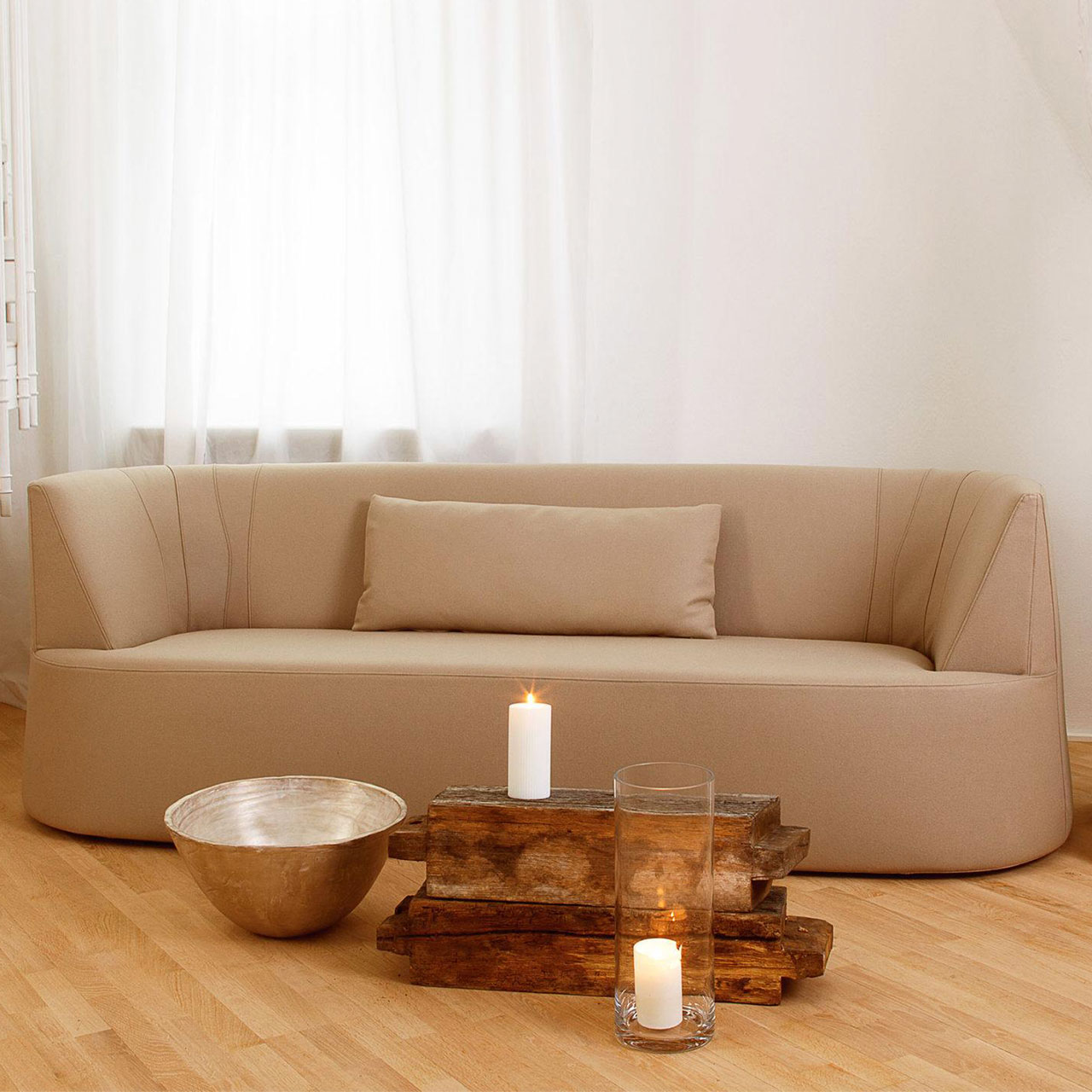 Ambientebild: Hellbraunes Ledersofa vor weiß durchscheinenden Vorhängen. 