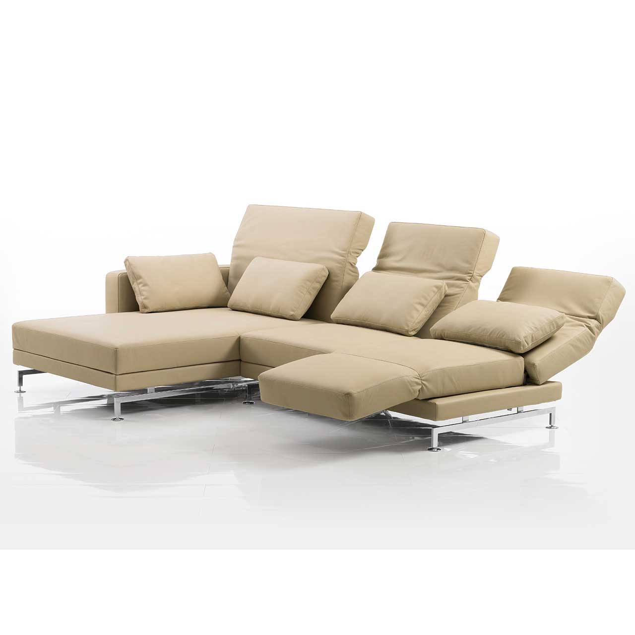Eckgarnitur mit breitem Longchair links und in beigem Leder. Die mittlere und rechte Rückenlehne sind teilweise abgesenkt. Die rechte Armlehne ist zur Fußstütze vorgeschwenkt.