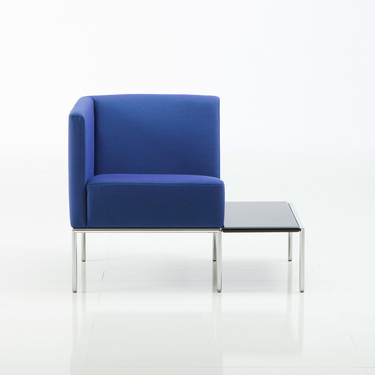 Mit blauem Stoff bezogener Sessel von brühl add1 mit einer Ablage auf der rechten Seite.