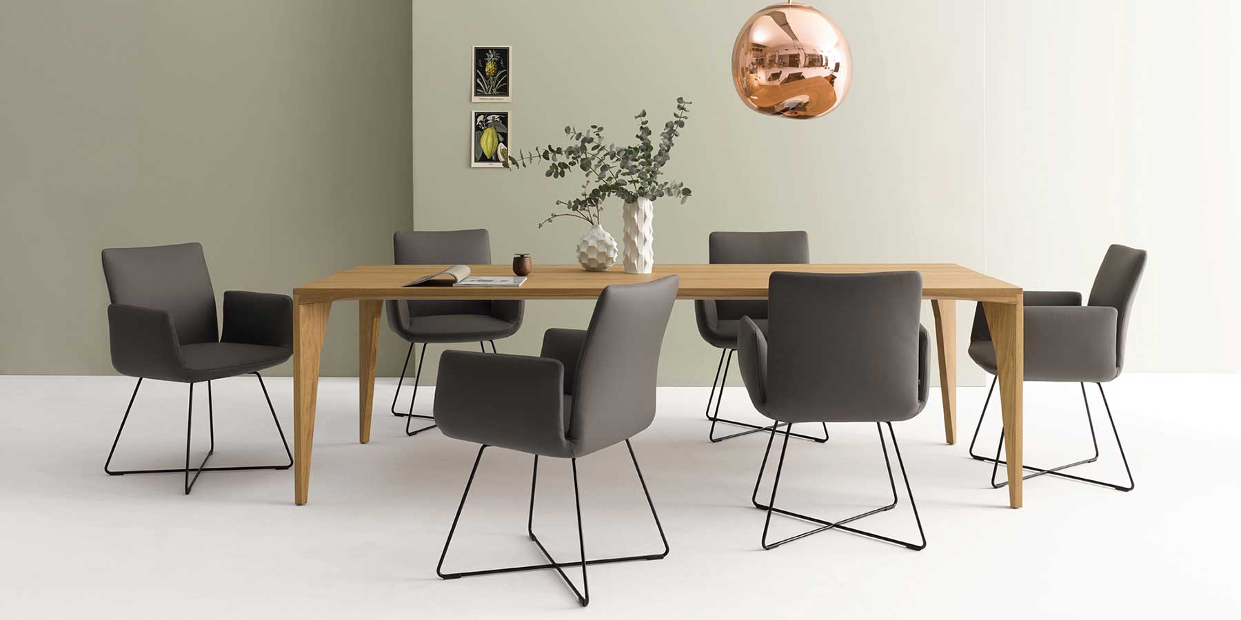 Sechs Stühle stehen um einen Holztisch herum. Die Stühle haben ein Drahtgestell und Armlehnen.