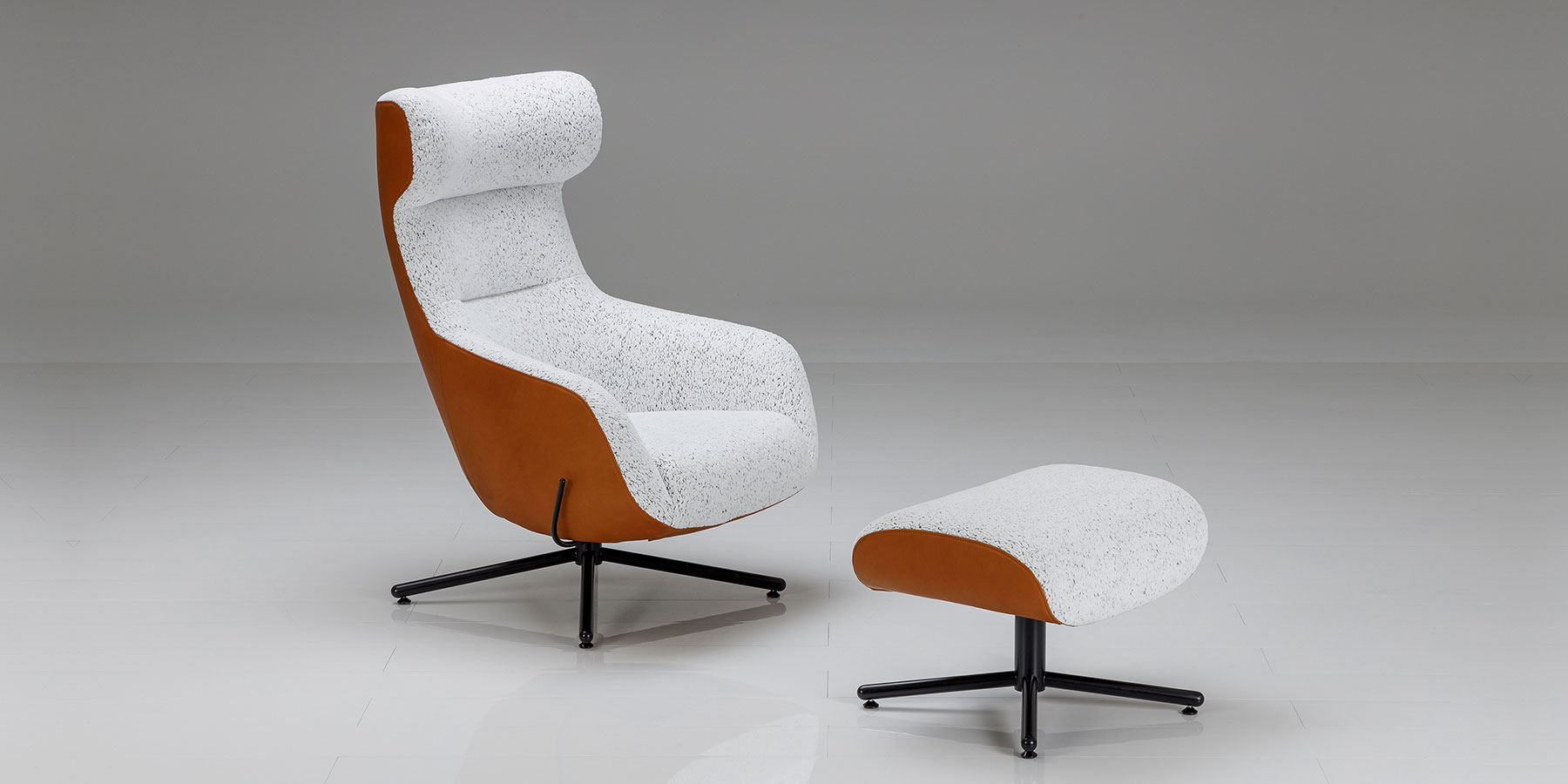 Weißer Hochlehnsessel mit Kreuzbasis in schwarz und dazu passendem Hocker.